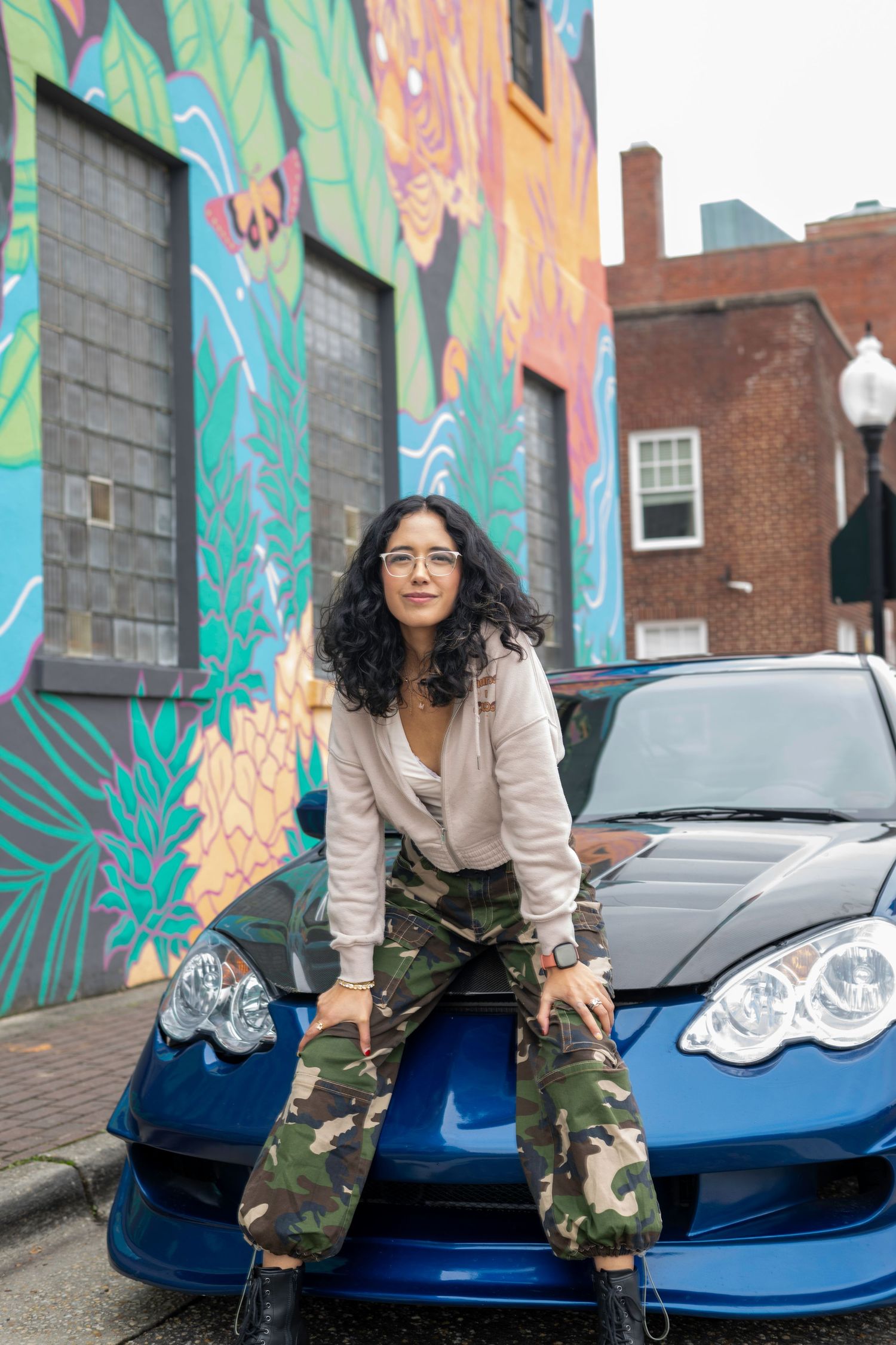Creative urban portrait of a woman posing beside a car and colorful mural