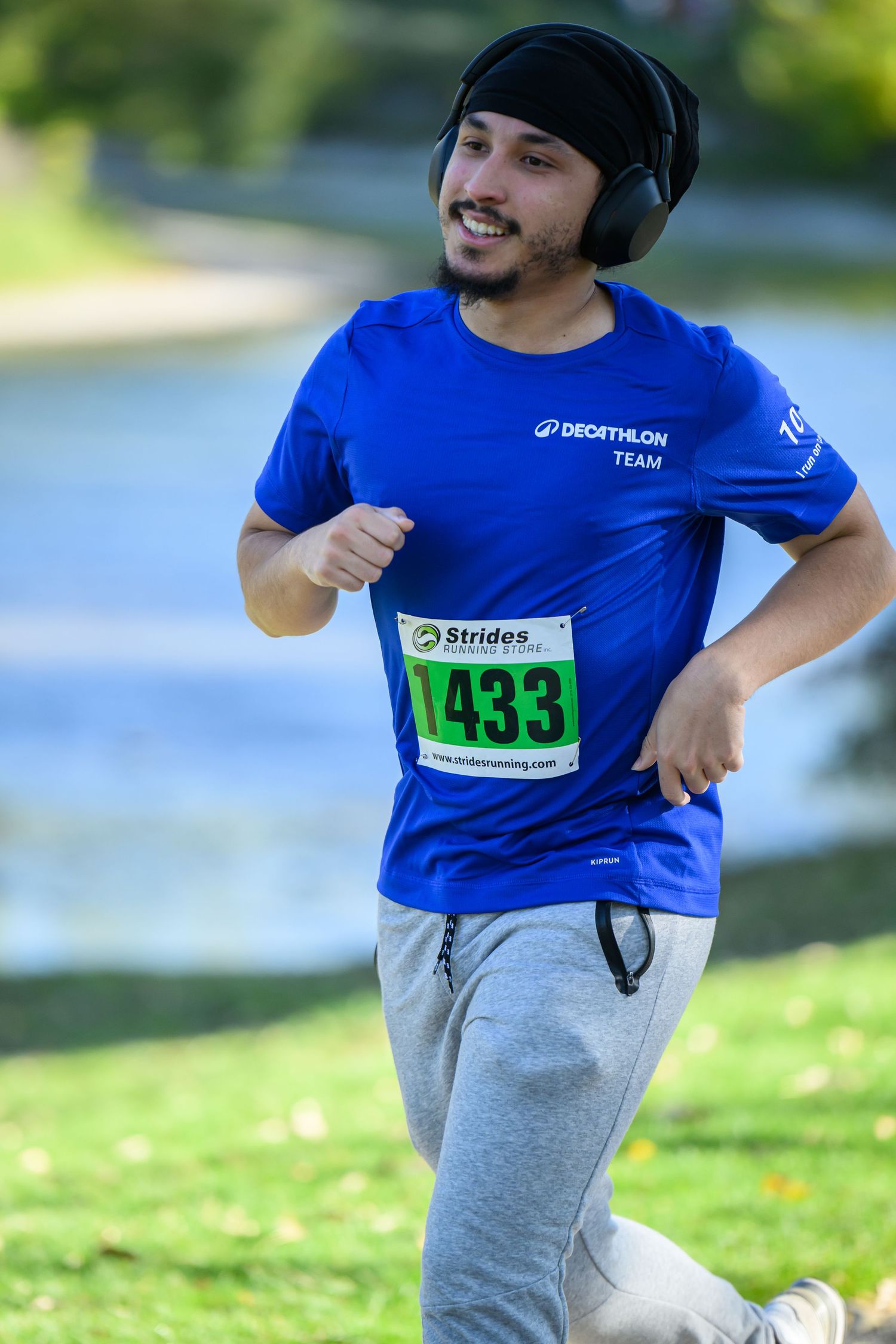Runner #1433 in blue Decathlon Team shirt and headphones jogging in a park race event.
