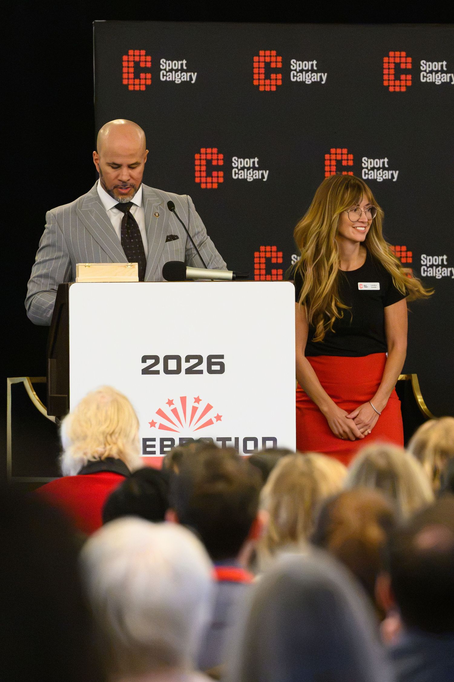 Two speakers at a Sport Calgary 2026 podium during a formal event presentation.