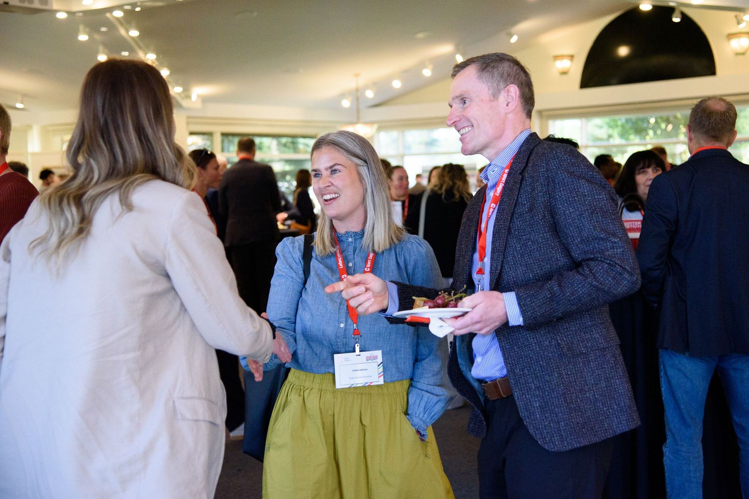 Smiling professionals shaking hands and networking at a busy indoor corporate event.