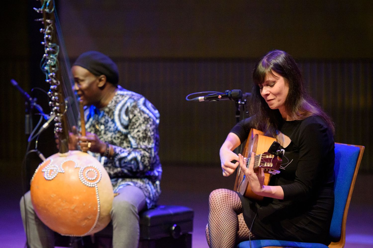 Two musicians perform on stage, one playing a kora and another playing acoustic guitar at a live concert.