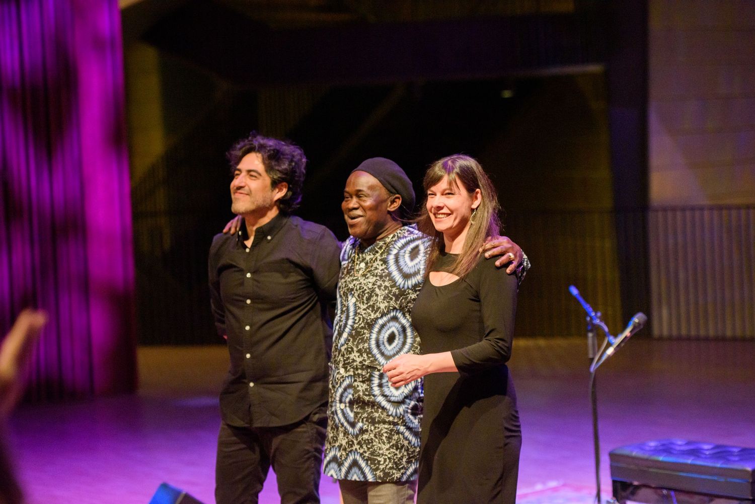 Three people smiling and posing together on a stage during an awards ceremony or live event performance.
