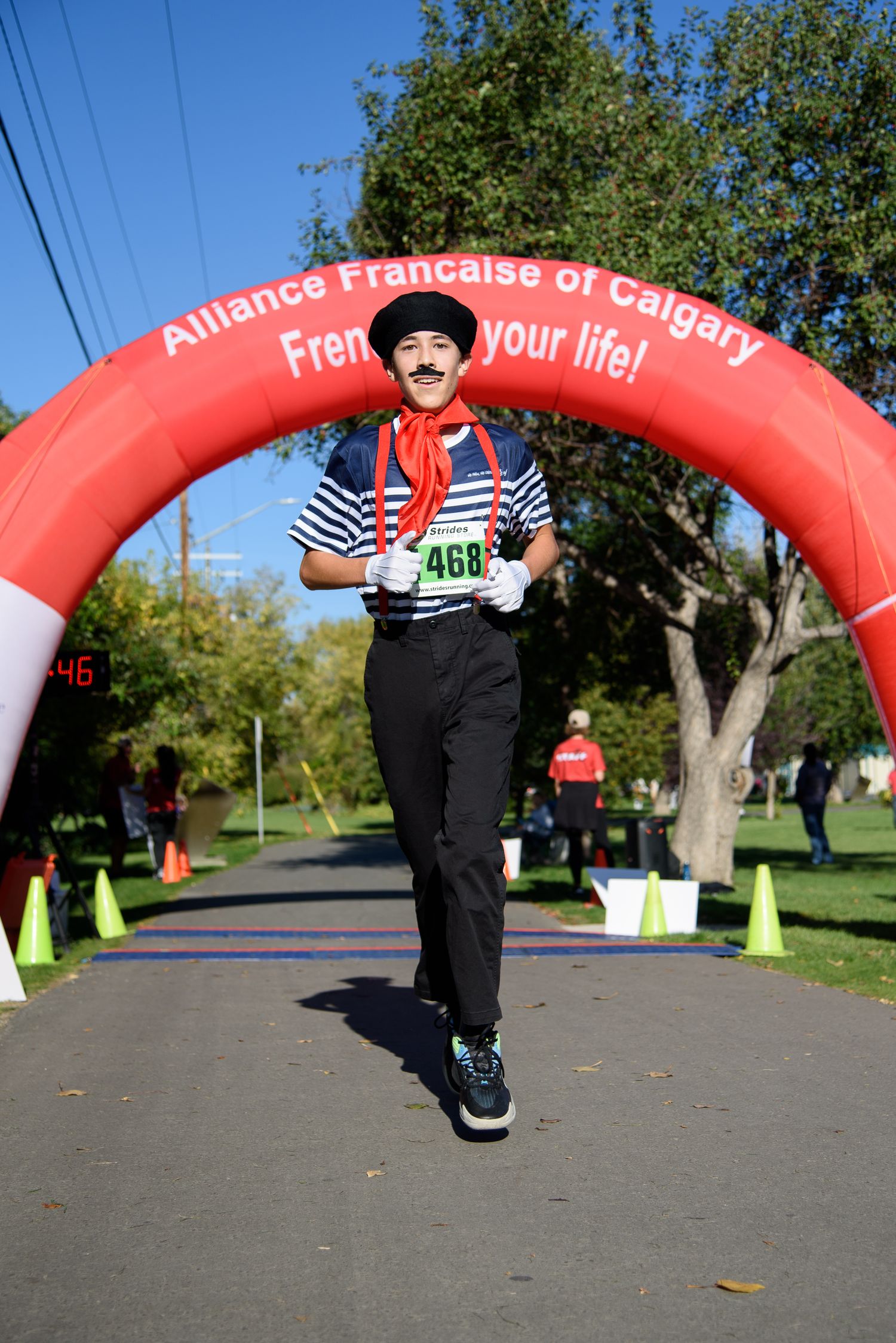 Runner in French mime costume crosses finish line at Alliance Francaise of Calgary race event on sunny day.