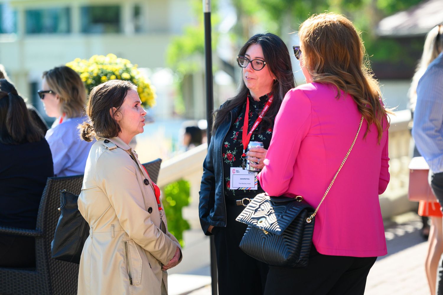Three professional women networking outdoors at a conference event on a sunny day.