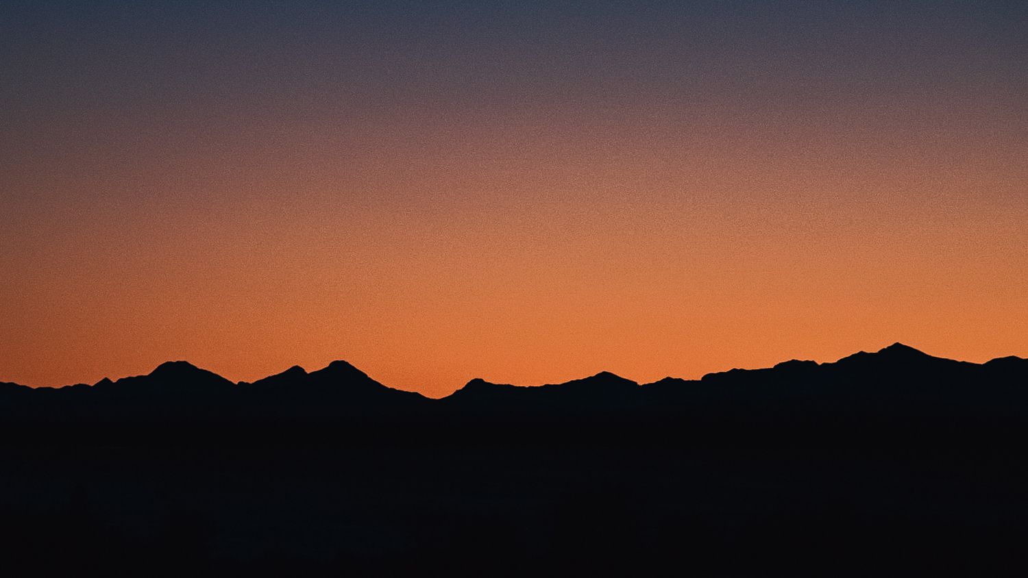 Silhouette of mountain range against vibrant orange and red sunset sky.