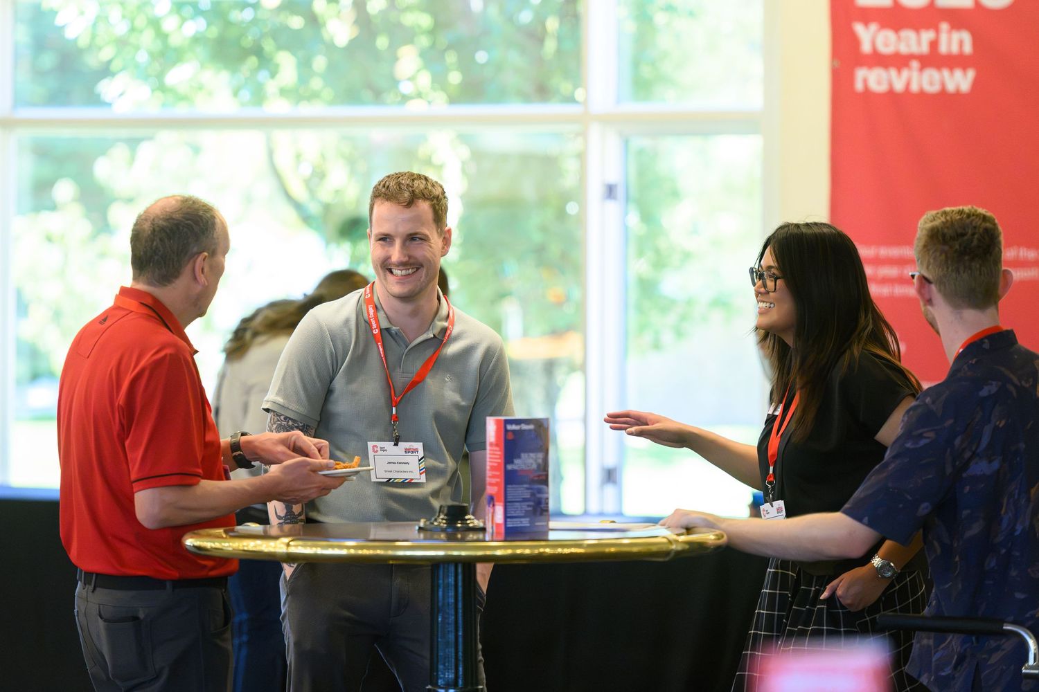 Professionals networking at a corporate event around a high-top table with branded displays.