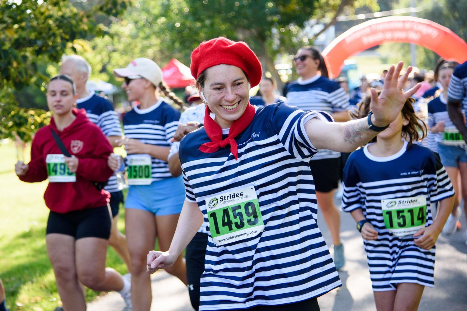 Runners in matching French-themed striped outfits and red berets participate in a fun charity race outdoors.