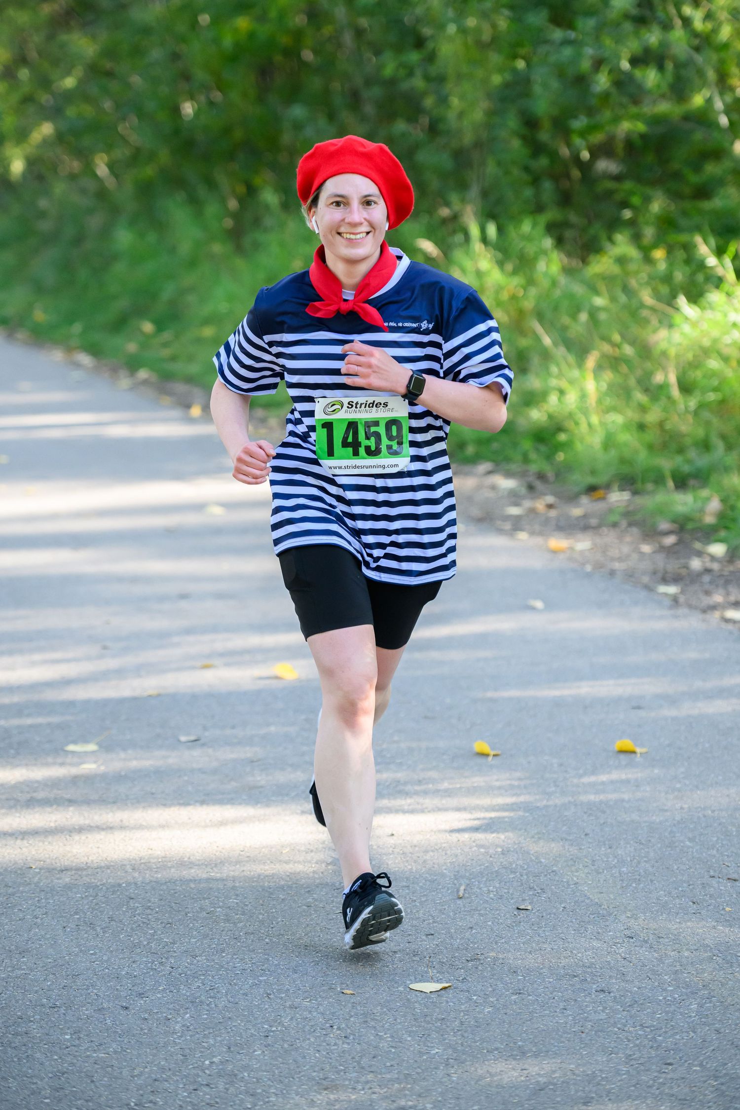 A smiling woman in a striped shirt and red beret runs a road race wearing bib number 1459.