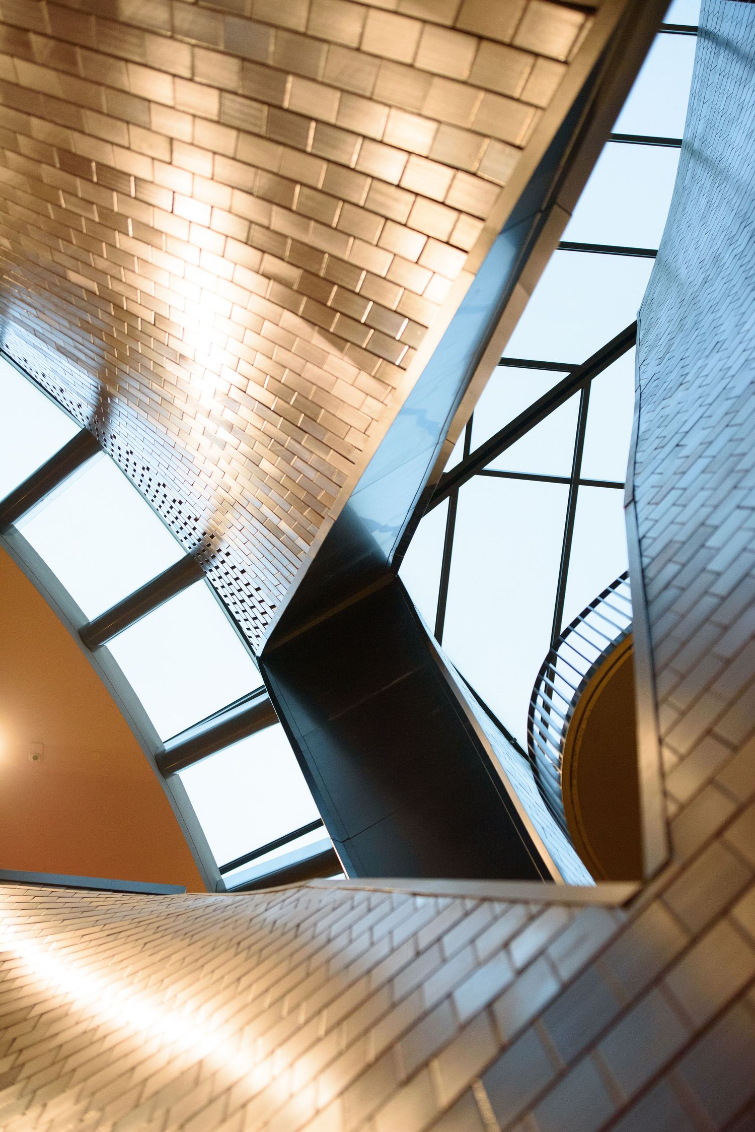Abstract architectural interior with brick walls, steel beams, and skylights creating geometric patterns in warm light.