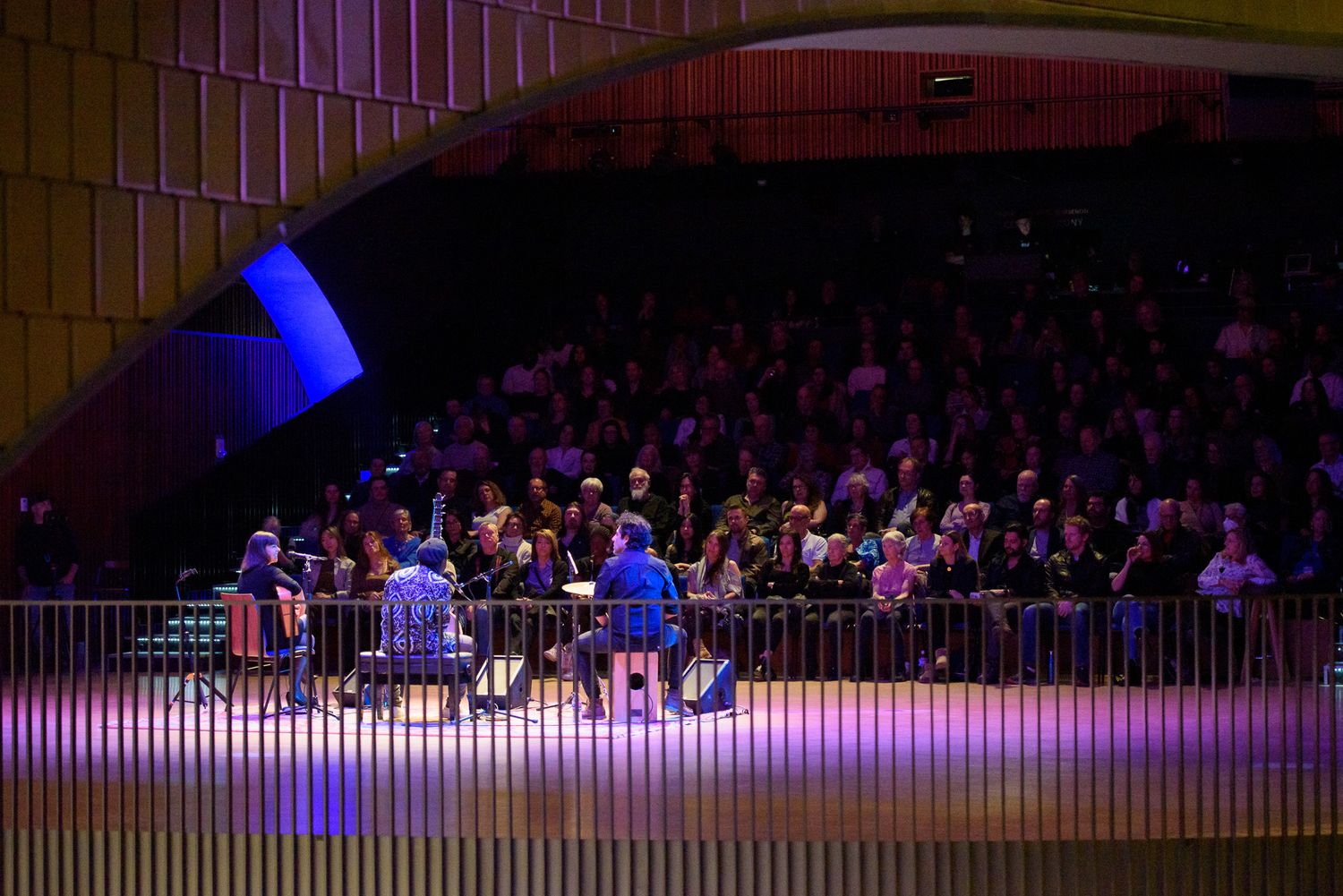 Performers on stage in modern concert hall with curved architecture and large audience in background.