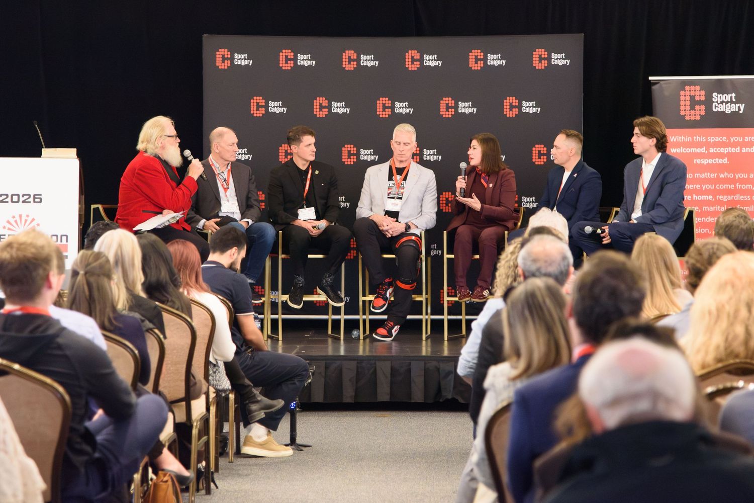 Panel of seven speakers presenting on stage at a professional conference event.