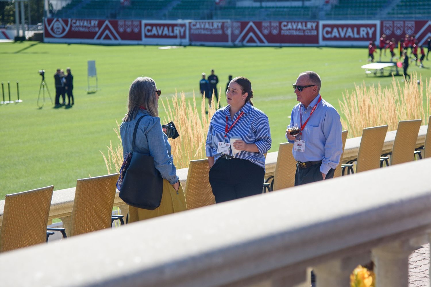 Three people networking at a Cavalry FC soccer stadium event on a sunny day.