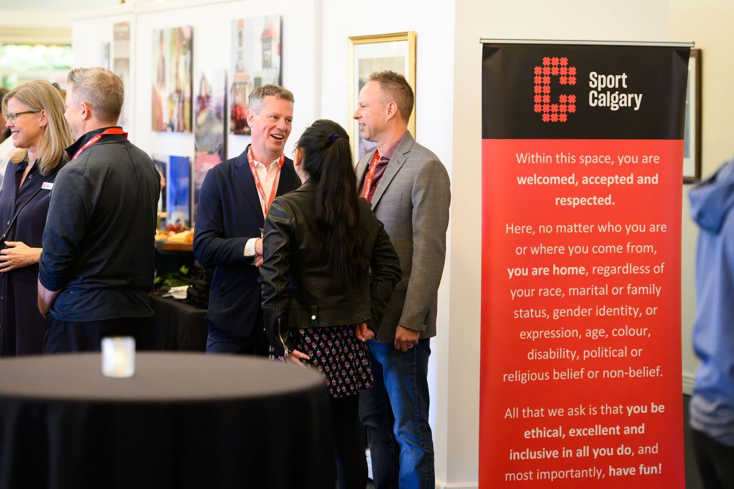 People networking at a Sport Calgary event beside an inclusive welcome banner.