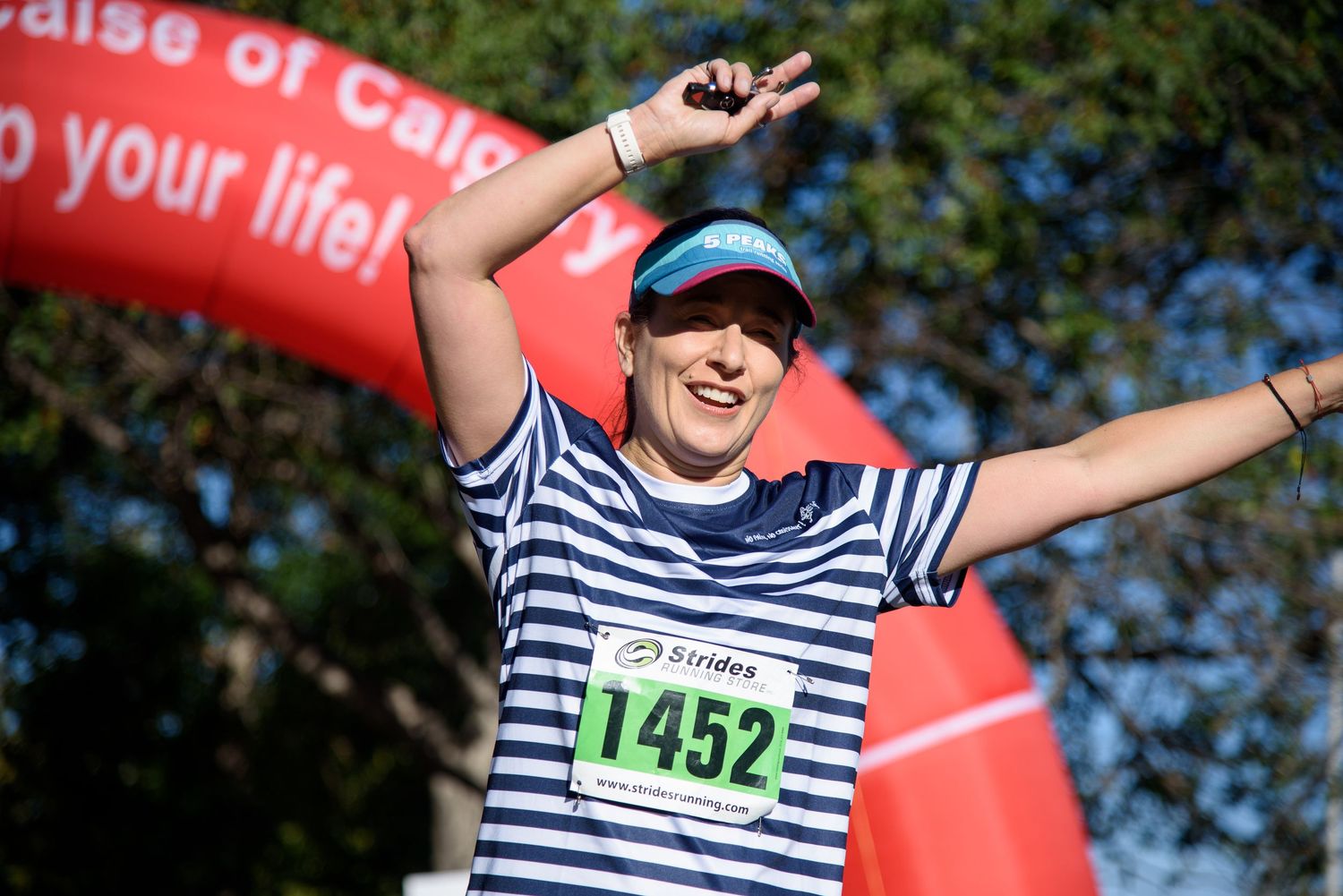 Runner #1452 celebrates crossing the finish line at a charity race event, arms raised in triumph.