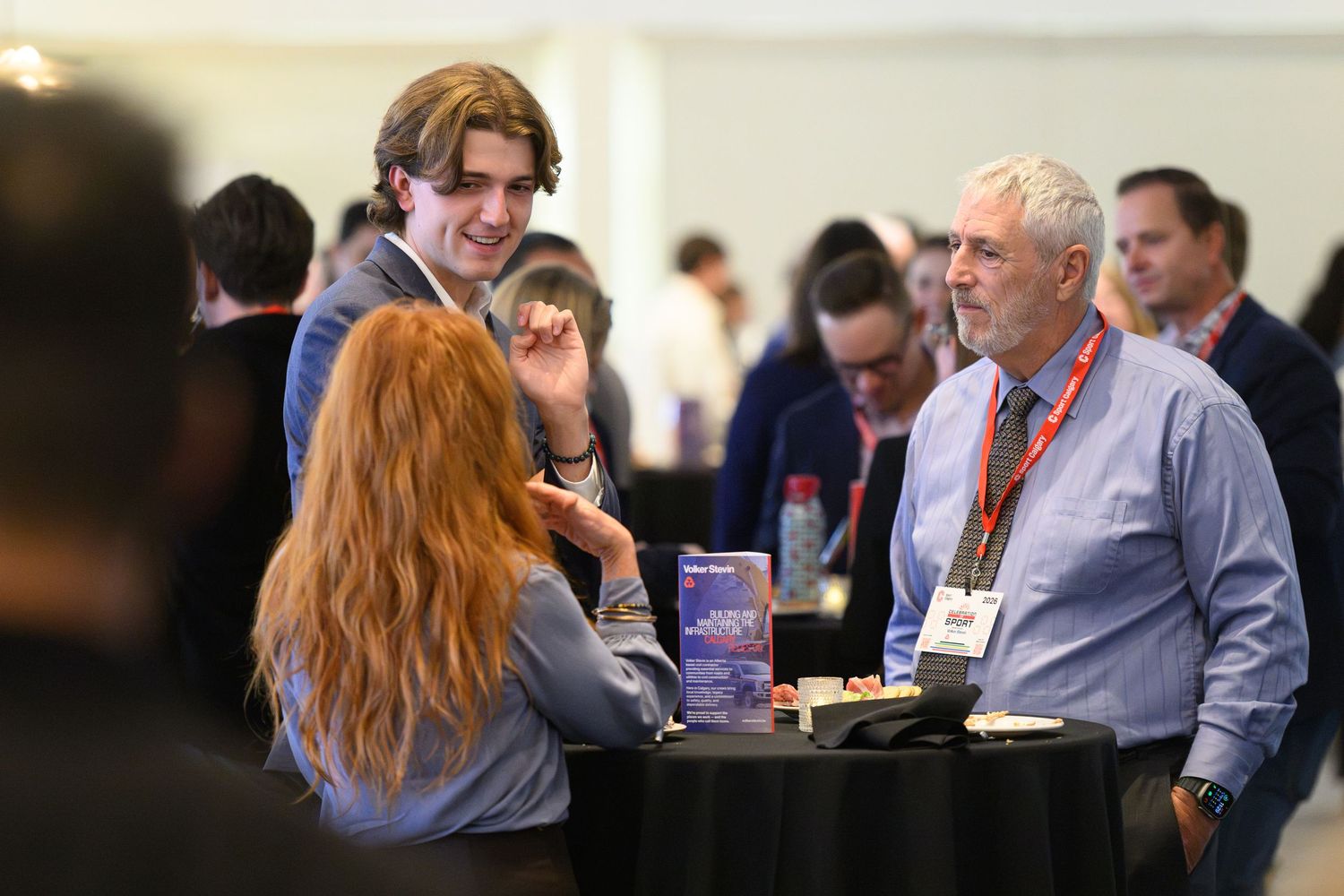 Professionals networking at a conference cocktail reception, standing around a high-top table in conversation.