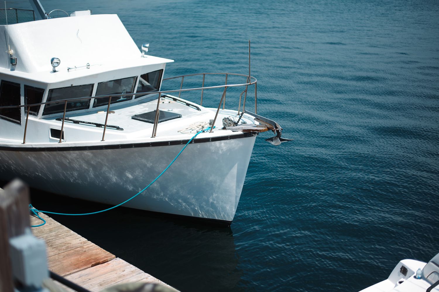 White fishing boat tied with blue rope to wooden dock on calm blue water.