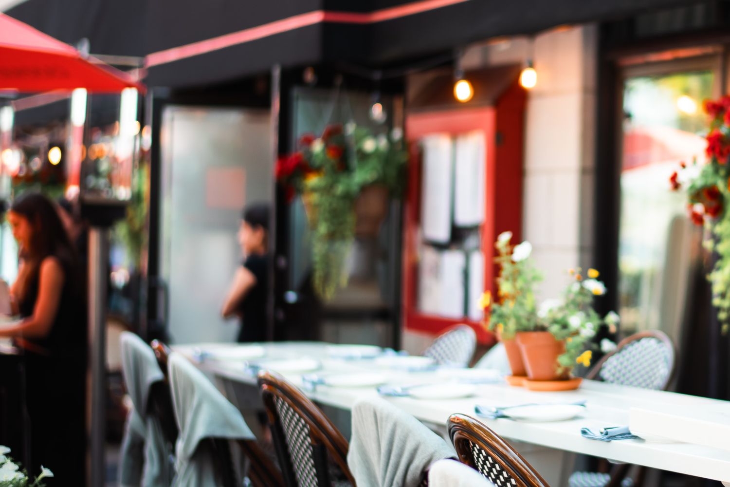 Elegant outdoor restaurant patio with white tablecloths, wicker chairs, and lush greenery.
