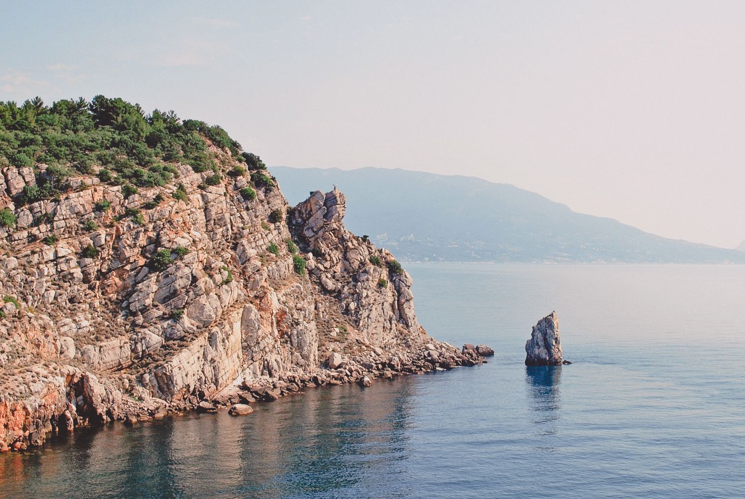 Scenic rocky coastline with green vegetation rising above calm blue sea waters.