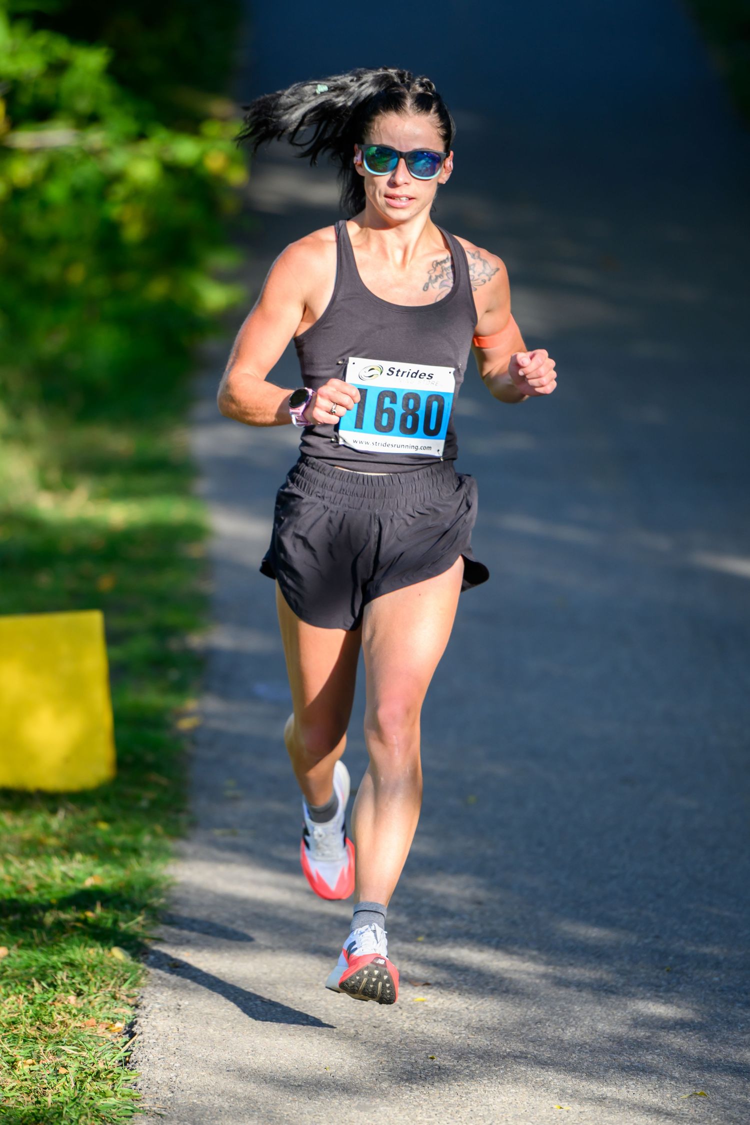 Woman runner wearing bib number 1680 and sunglasses racing on a paved path during an outdoor road race.