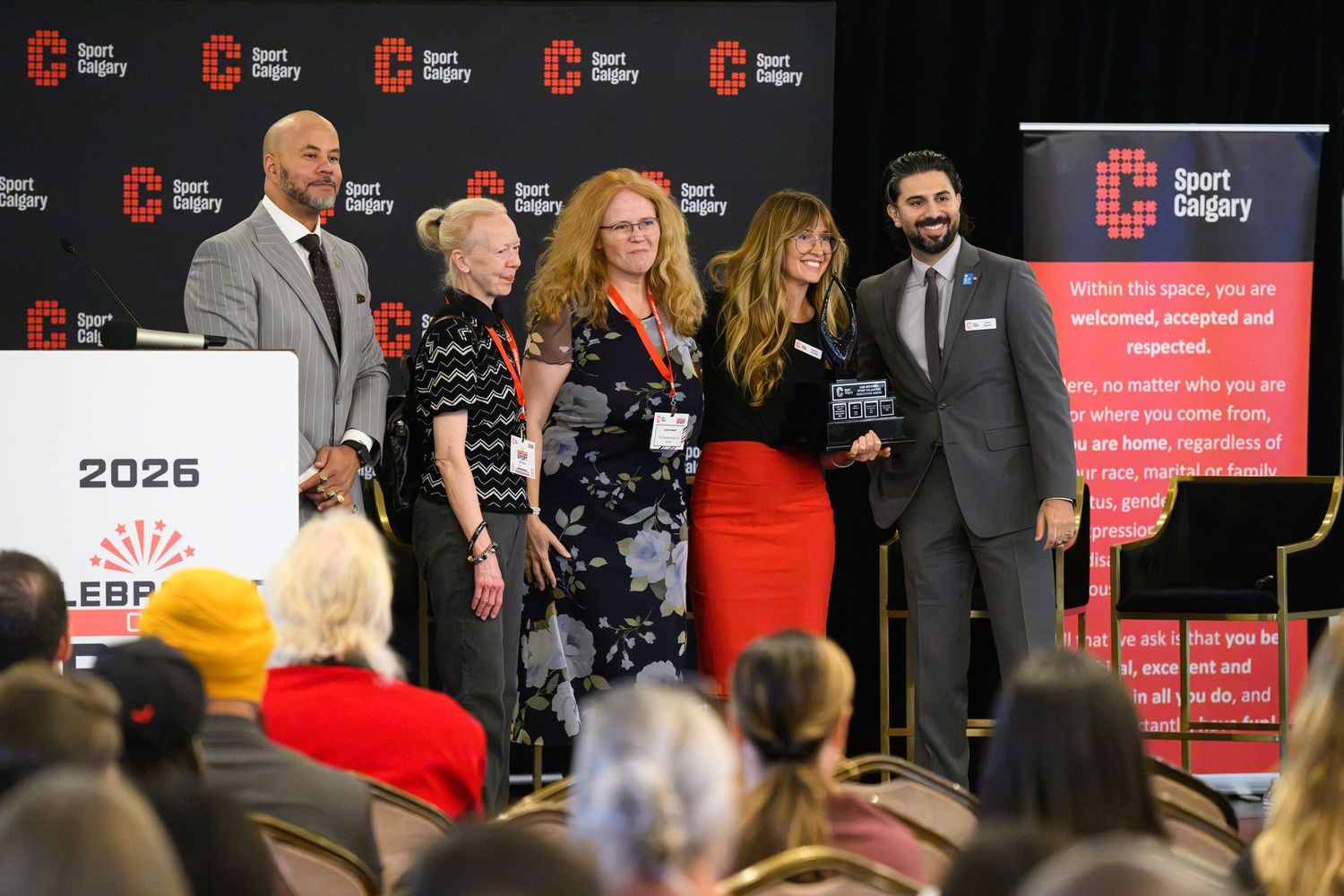 Group of people standing on stage at a Sport Calgary awards ceremony with a 2026 banner visible in the background.