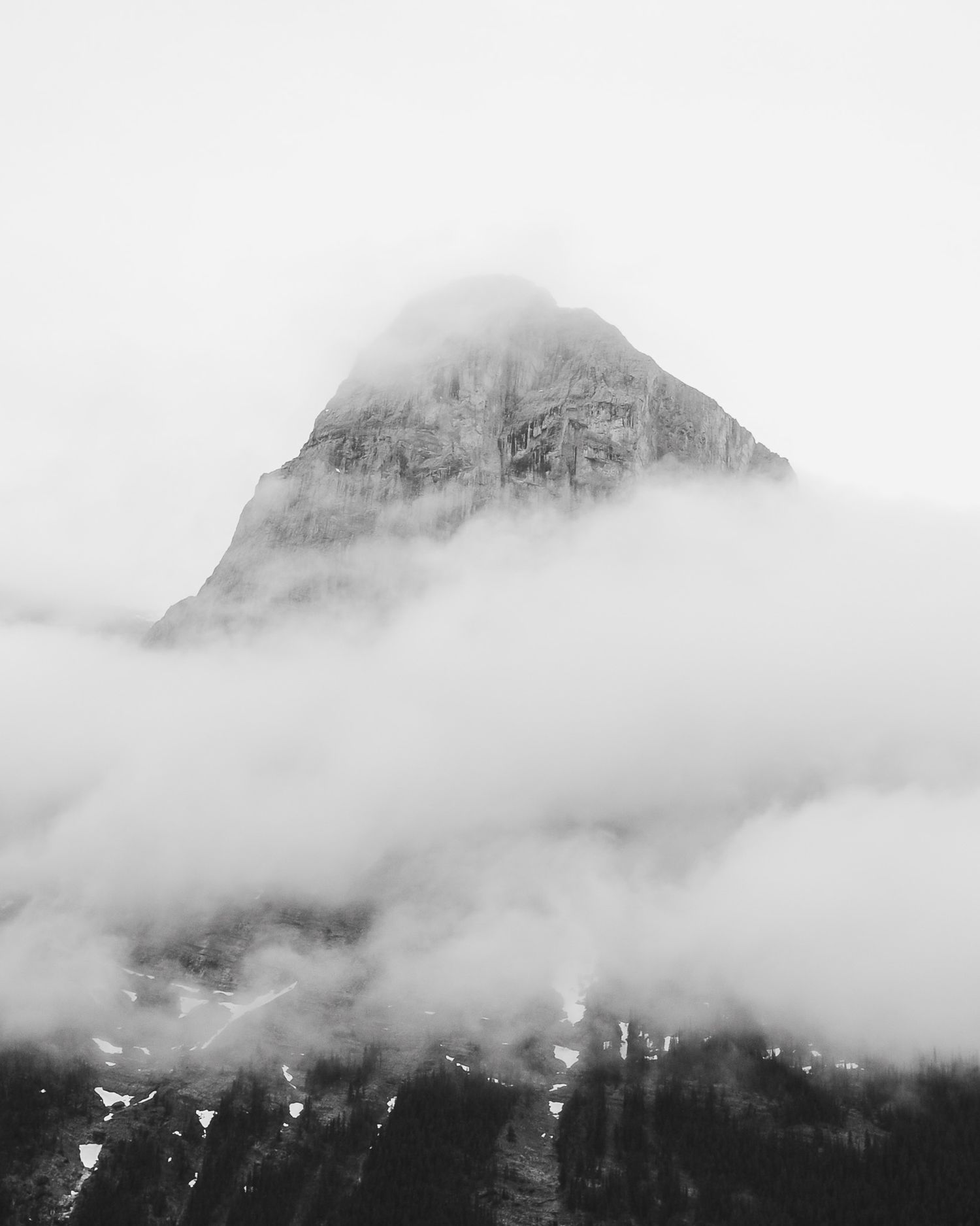 Dramatic black and white image of a mountain summit emerging through thick clouds.