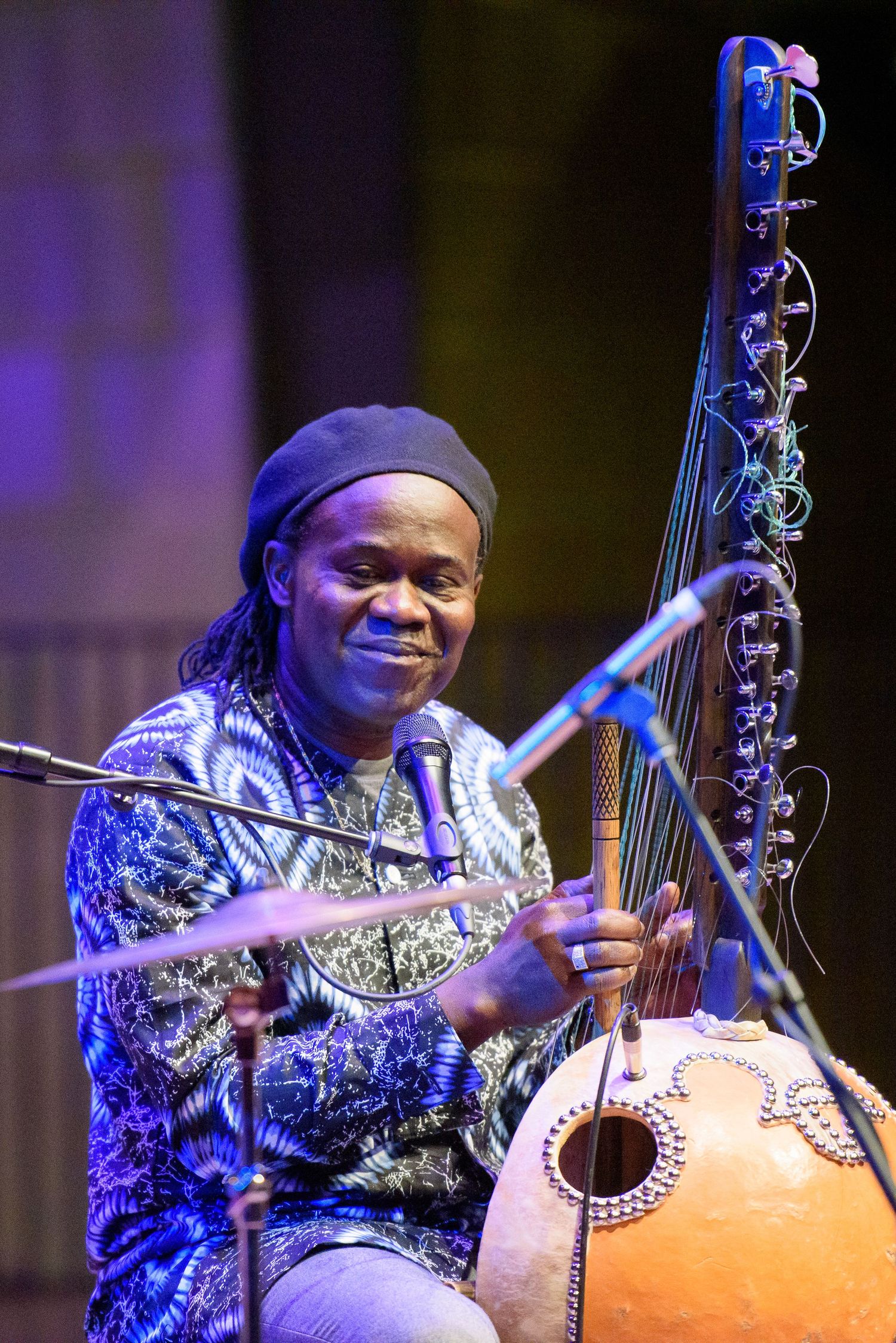 Musician playing a kora, a West African string instrument, on stage with microphones during a live performance.