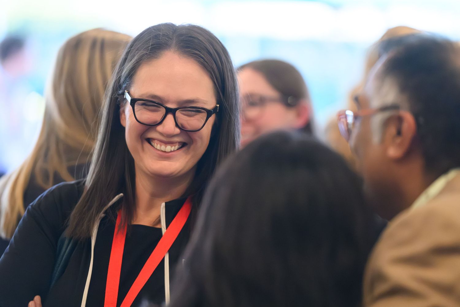 A smiling woman wearing glasses and a red lanyard engages in conversation at a professional networking event.