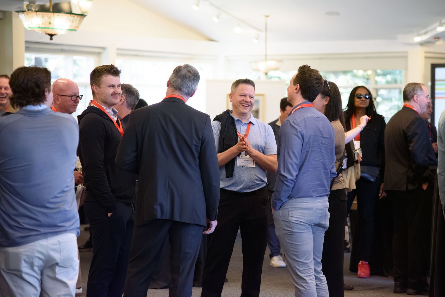 Professionals networking at an indoor corporate event, socializing in a bright room wearing business casual attire.