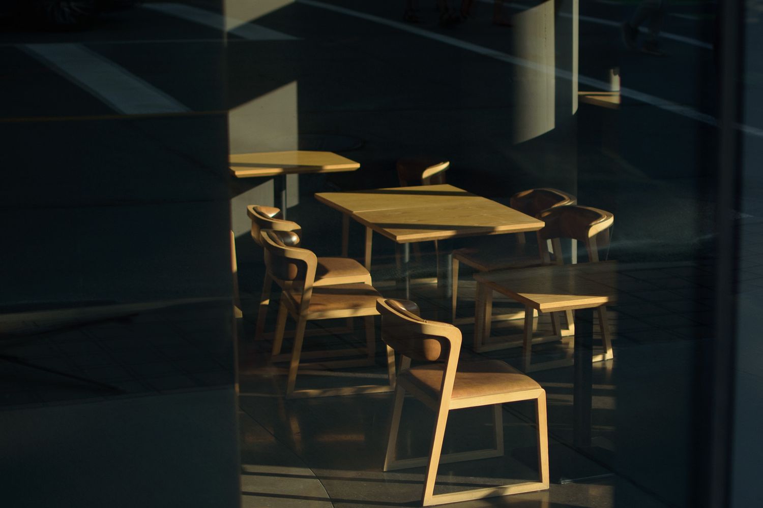 Wooden chairs and tables bathed in warm golden sunlight inside a modern cafe.