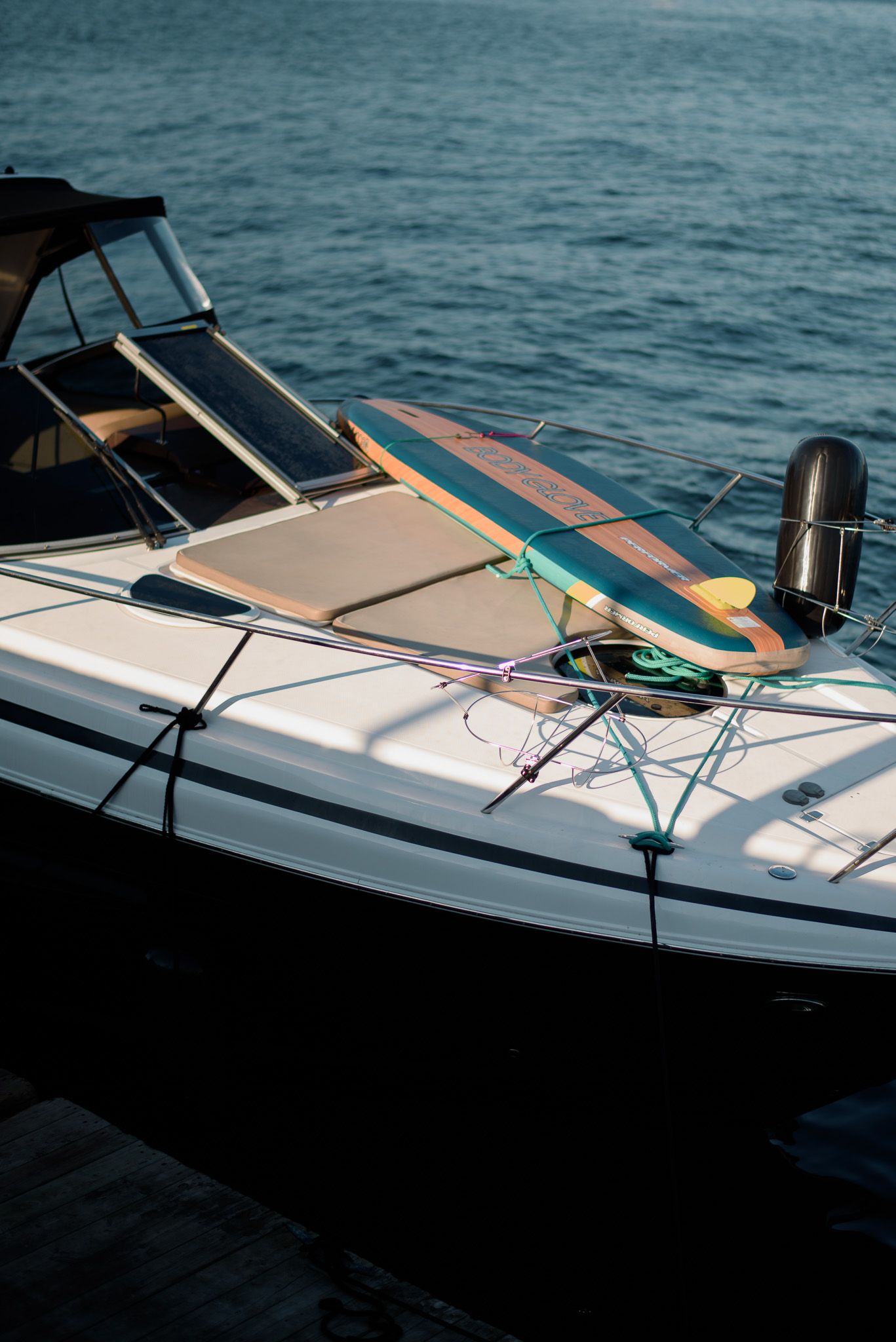 Wooden surfboard resting on bow of white luxury yacht docked at marina.