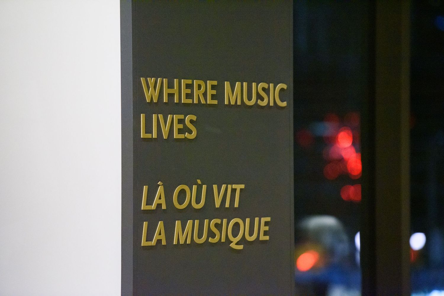Bilingual sign reading Where Music Lives and La Ou Vit La Musique in gold letters on a dark wall.