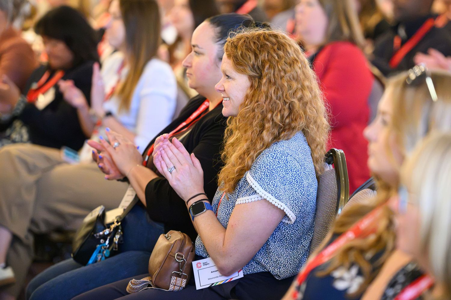 Engaged audience members applauding at a professional conference event in a crowded venue.