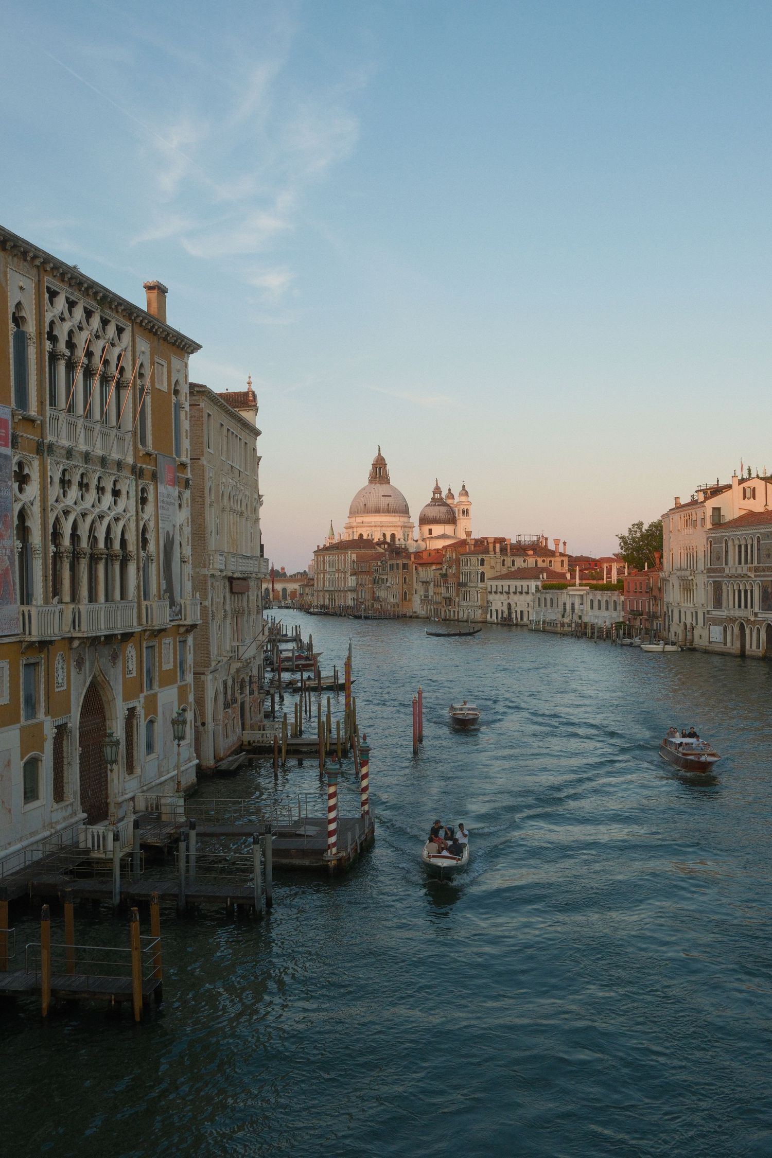 Golden hour view of Venice Grand Canal with boats and Santa Maria della Salute basilica in the background.
