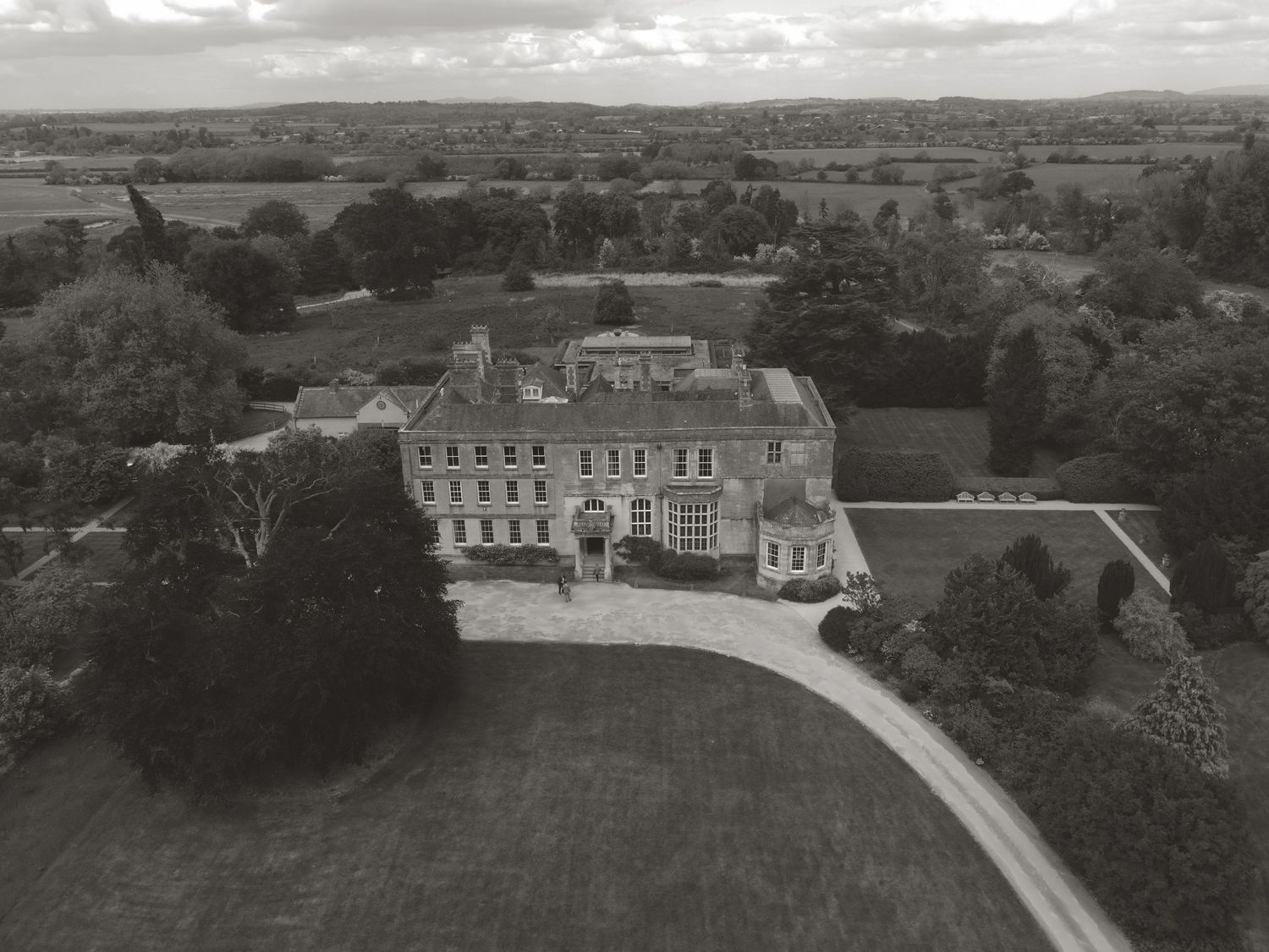 Black and white aerial drone photo of a grand Georgian country manor house surrounded by parkland.