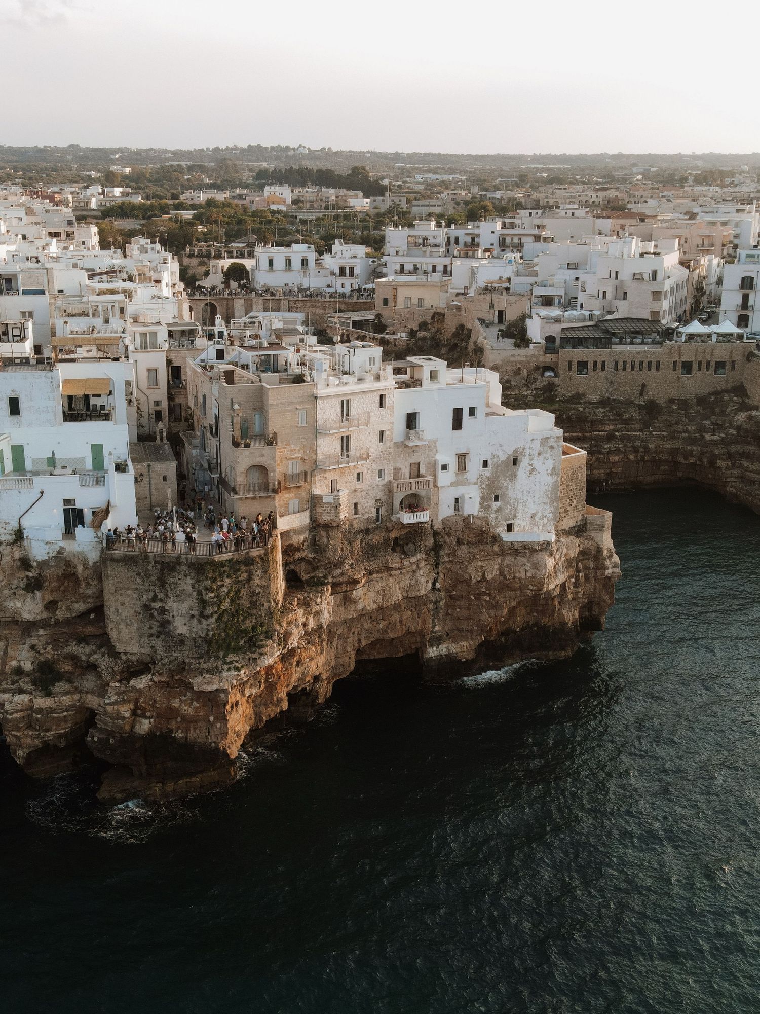 Aerial view of white-washed buildings perched dramatically on rocky cliffs above the sea in Polignano a Mare.