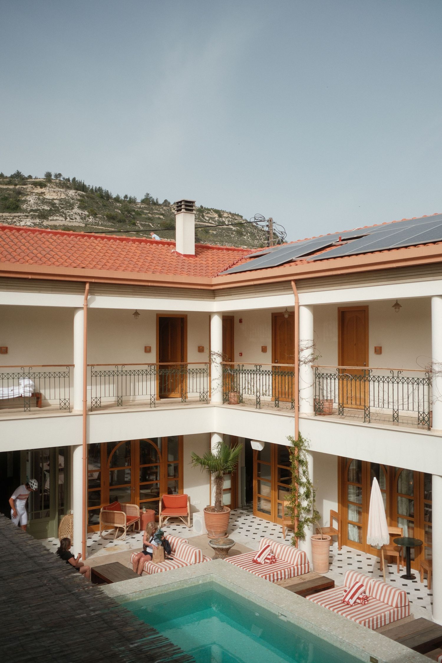 Charming hotel courtyard with swimming pool, striped loungers, and two-story balconied facade in a hillside town.
