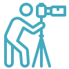 Teal blue line art icon of a videographer using a camera on a tripod.