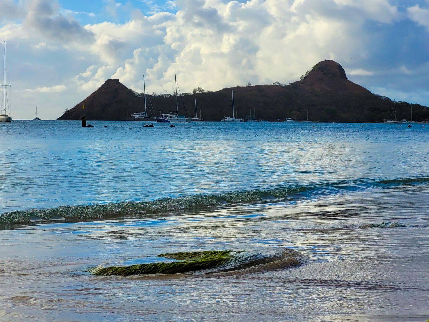 Calm Caribbean bay with sailboats and twin volcanic peaks under dramatic clouds in Saint Lucia.