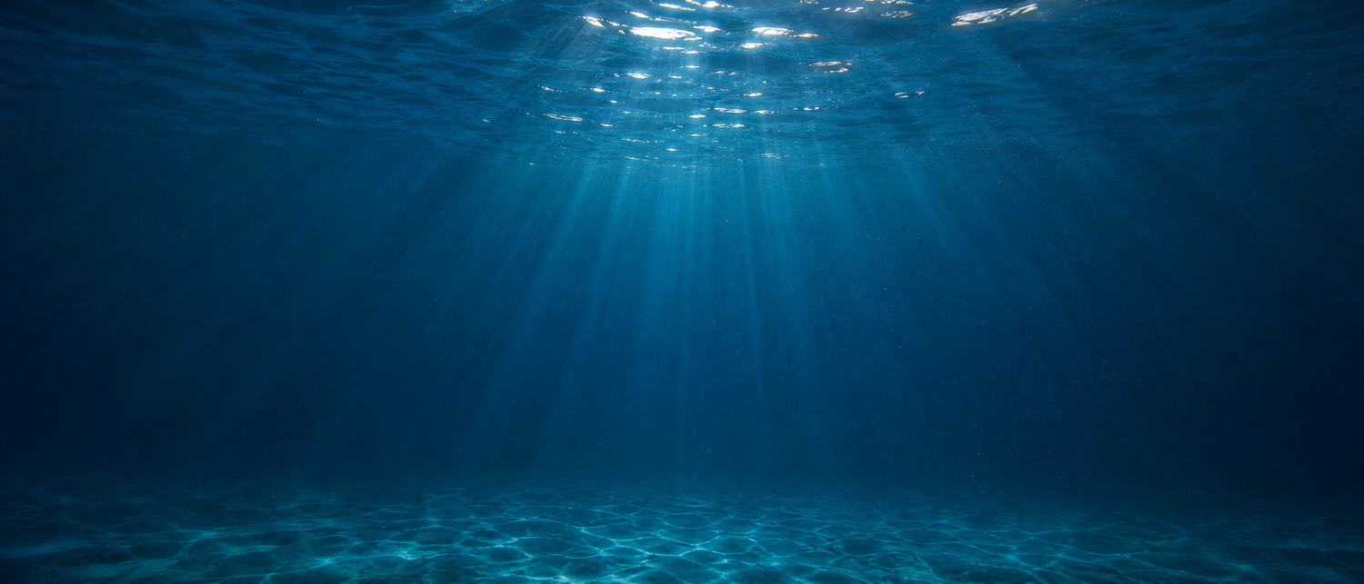 Sunlight rays filtering through clear blue ocean water illuminating sandy seafloor in stunning underwater scene.