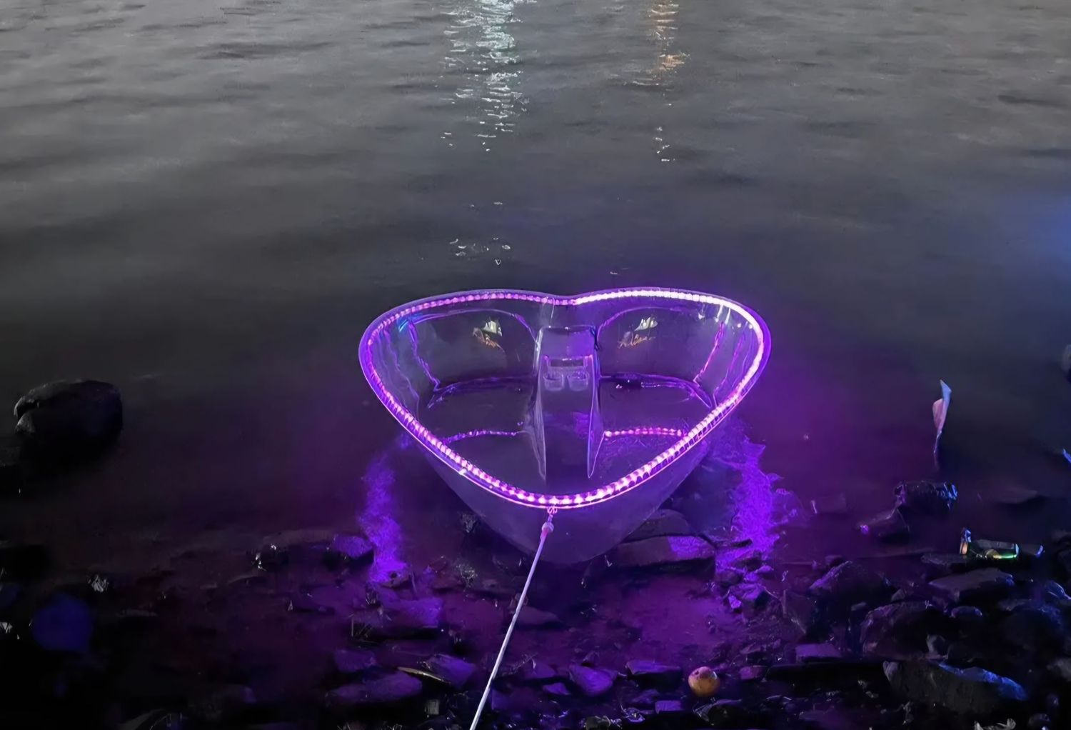 Heart-shaped boat with purple LED lights glowing on water at night.