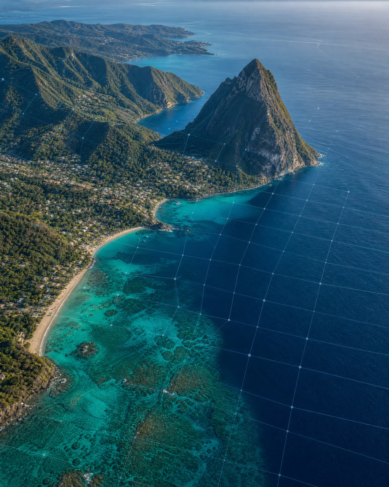 Aerial view of St. Lucia's Petit Piton mountain rising above a turquoise coral reef coastline and beach.