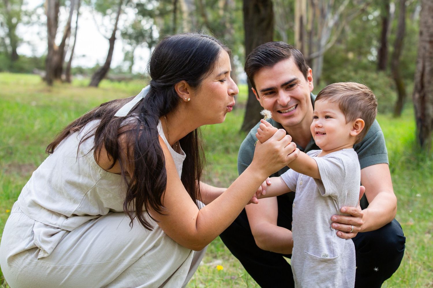 A happy young family with mother, father, and toddler son enjoying a fun outdoor moment together in a green park.