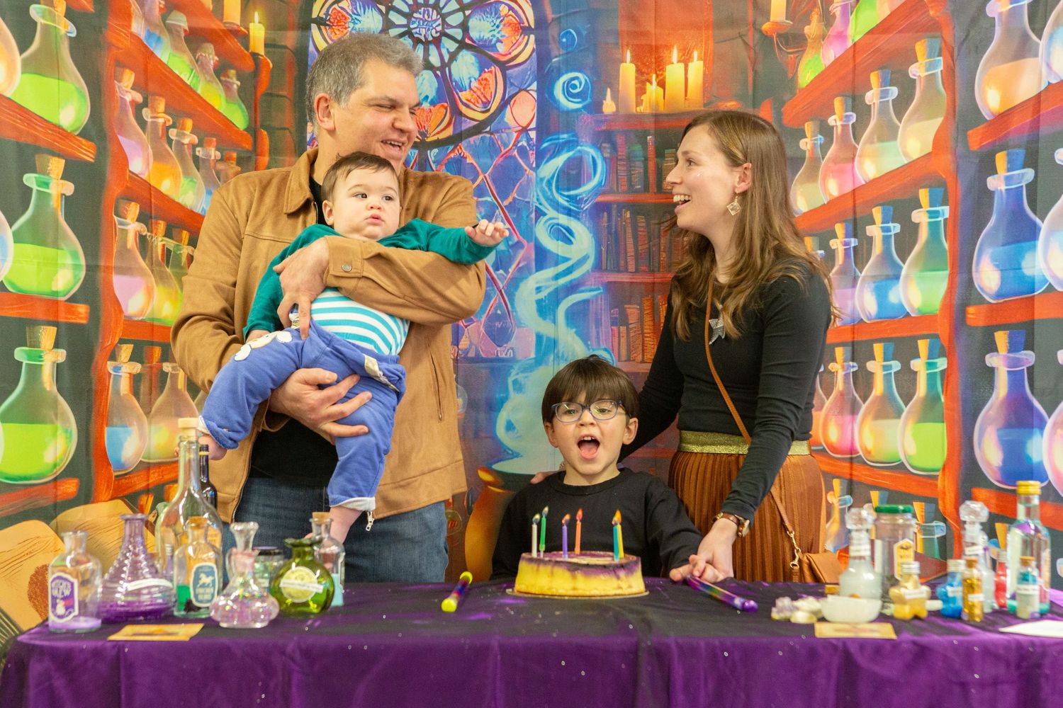Family of four celebrates a birthday at a colorful wizard-themed party with candles and potion bottles.
