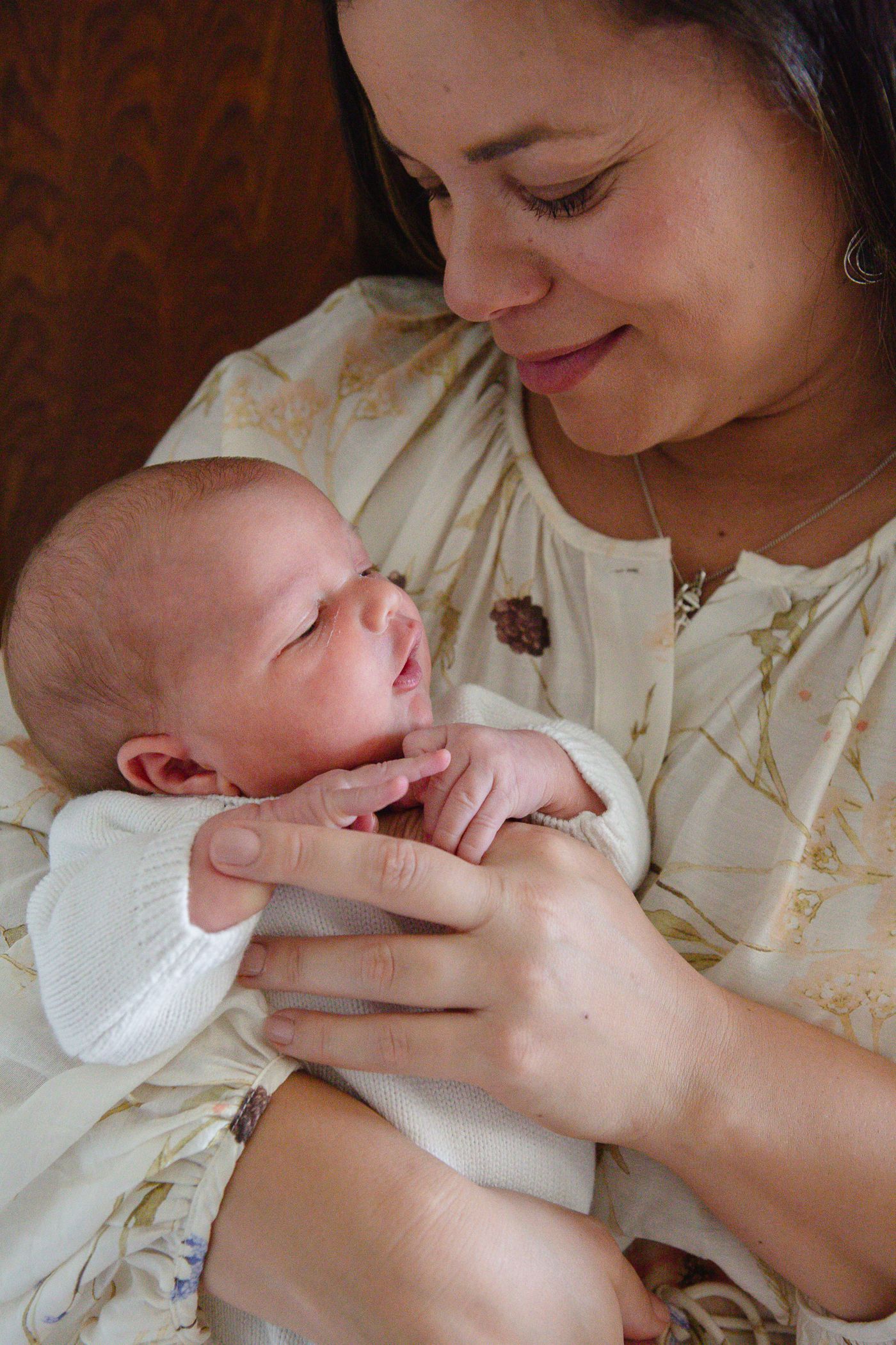 A smiling mother tenderly holds her newborn baby wrapped in white cloth, sharing a precious bonding moment.