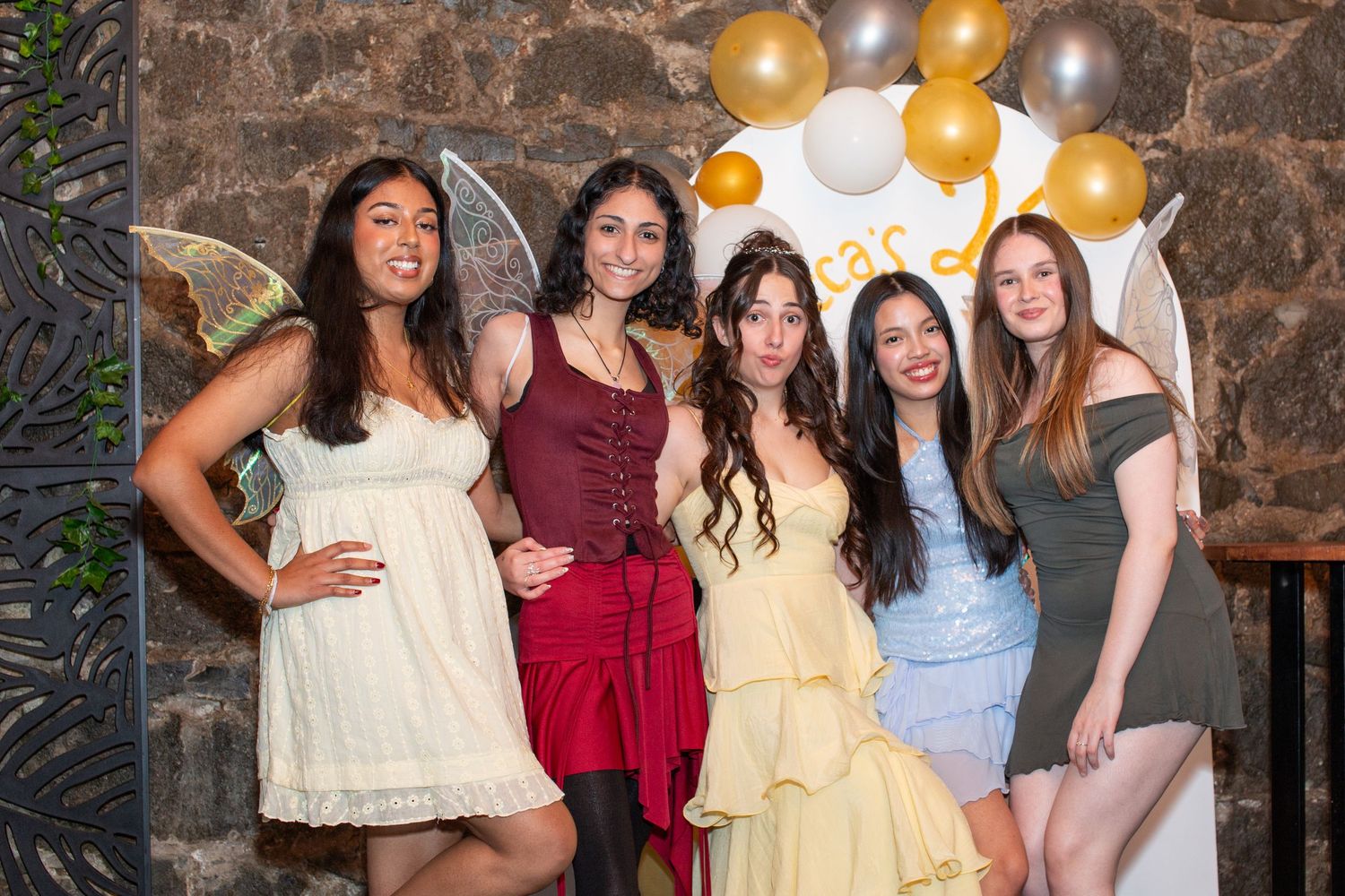Five young women pose together at a fairy-themed party with balloons and gold decorations.