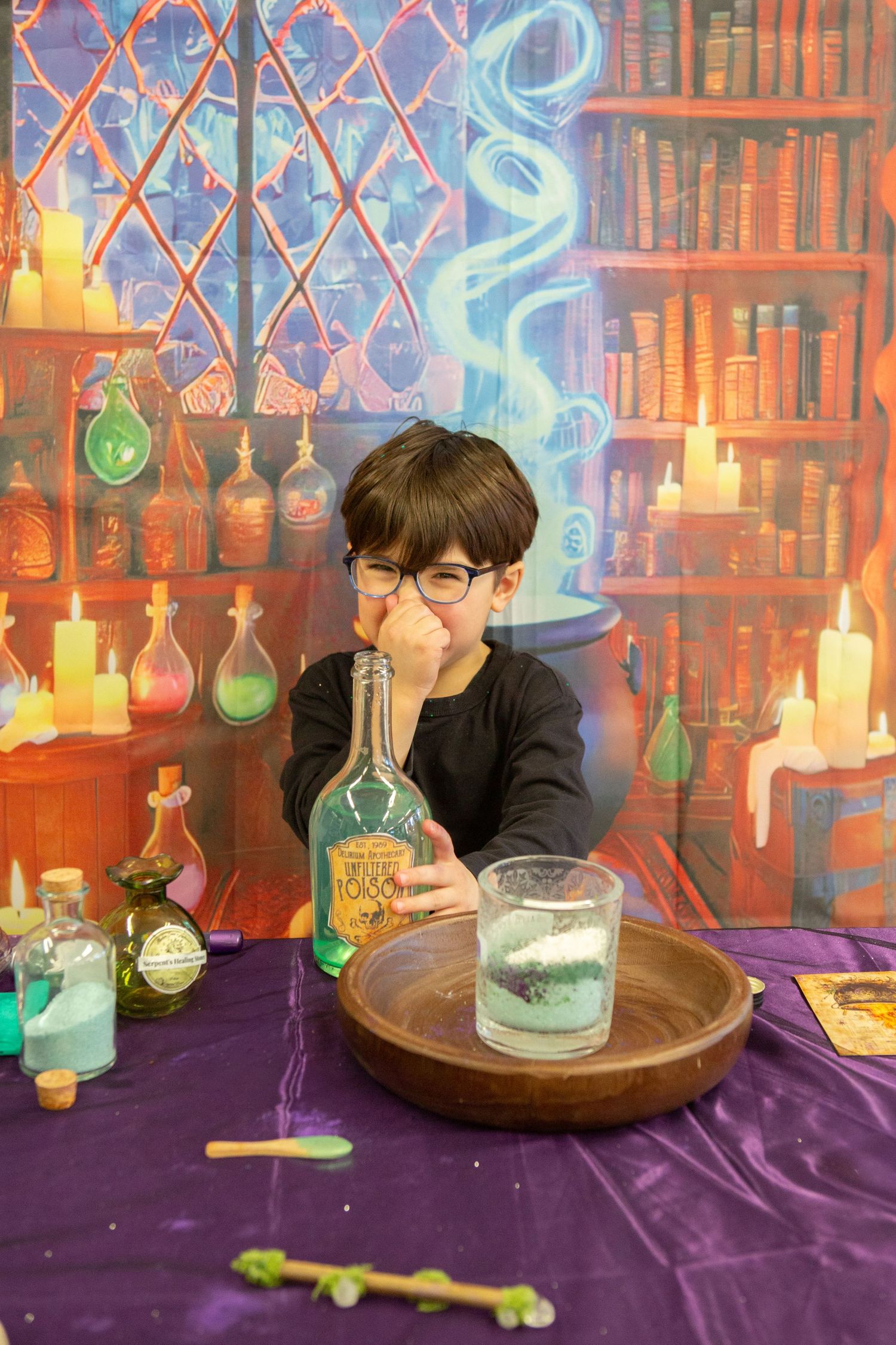 Young boy in glasses smells a potion bottle at a magical wizard-themed photo shoot.