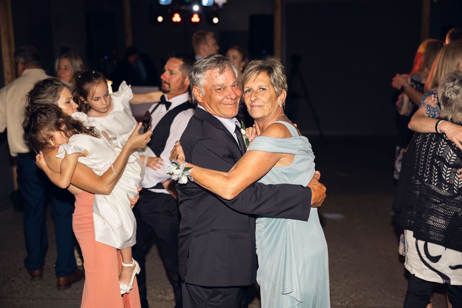 An older couple dances together on the dance floor at a wedding reception while flower girls in white dresses play nearby.