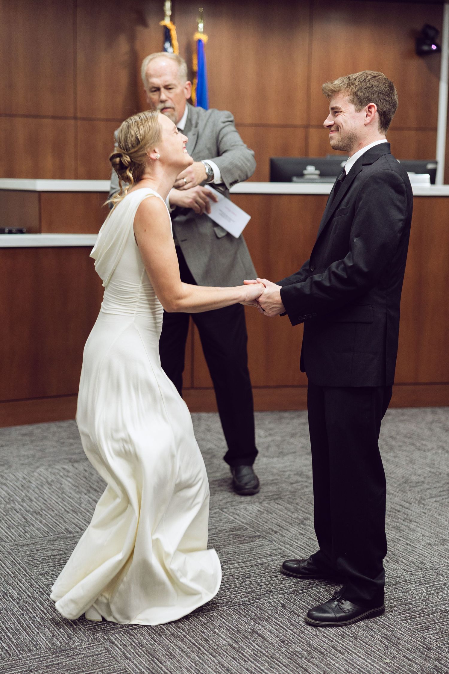 Bride leans back laughing while holding the groom's hands as the officiant looks on during a joyful courthouse wedding.