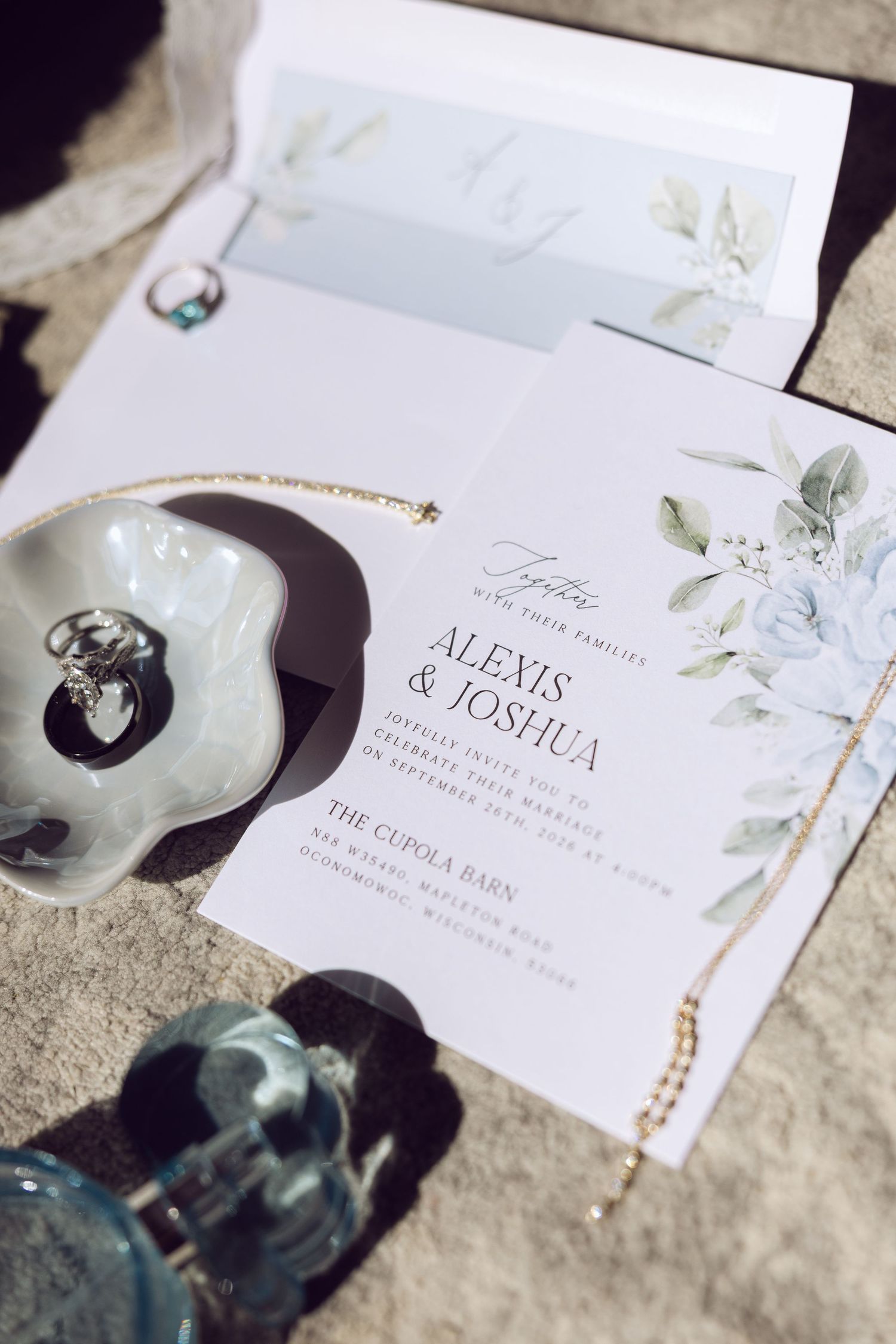 Wedding invitation for Alexis and Joshua at The Cupola Barn styled with floral details, rings in a shell dish, and jewelry.