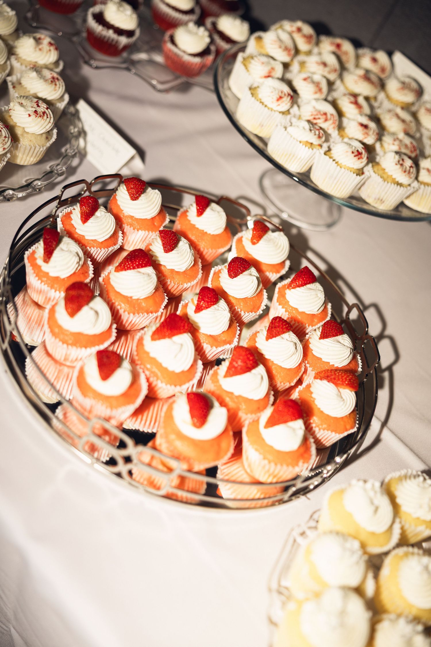 Tiered display of cupcakes topped with white frosting and fresh strawberries at a wedding dessert table.